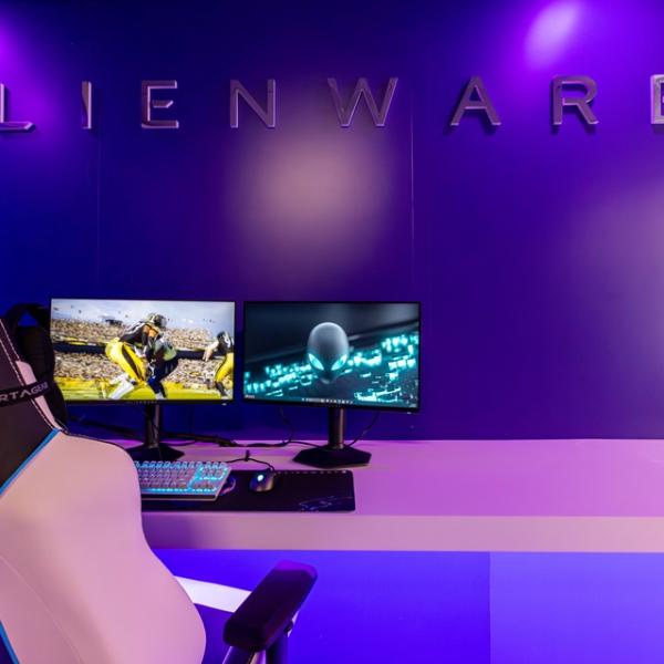 Gaming Chair and dual monitors in a pink and purple lit room with "Alienware" on wall