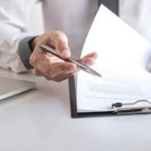 Hand with pen flipping through papers on a clipboard
