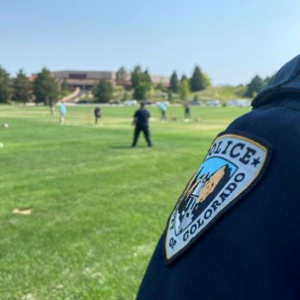 Business school field with staff playing cricket, CUPD officer in foreground
