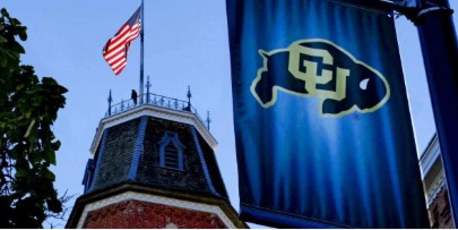 CU Banner on flagpole with US Flag on CU Building in background