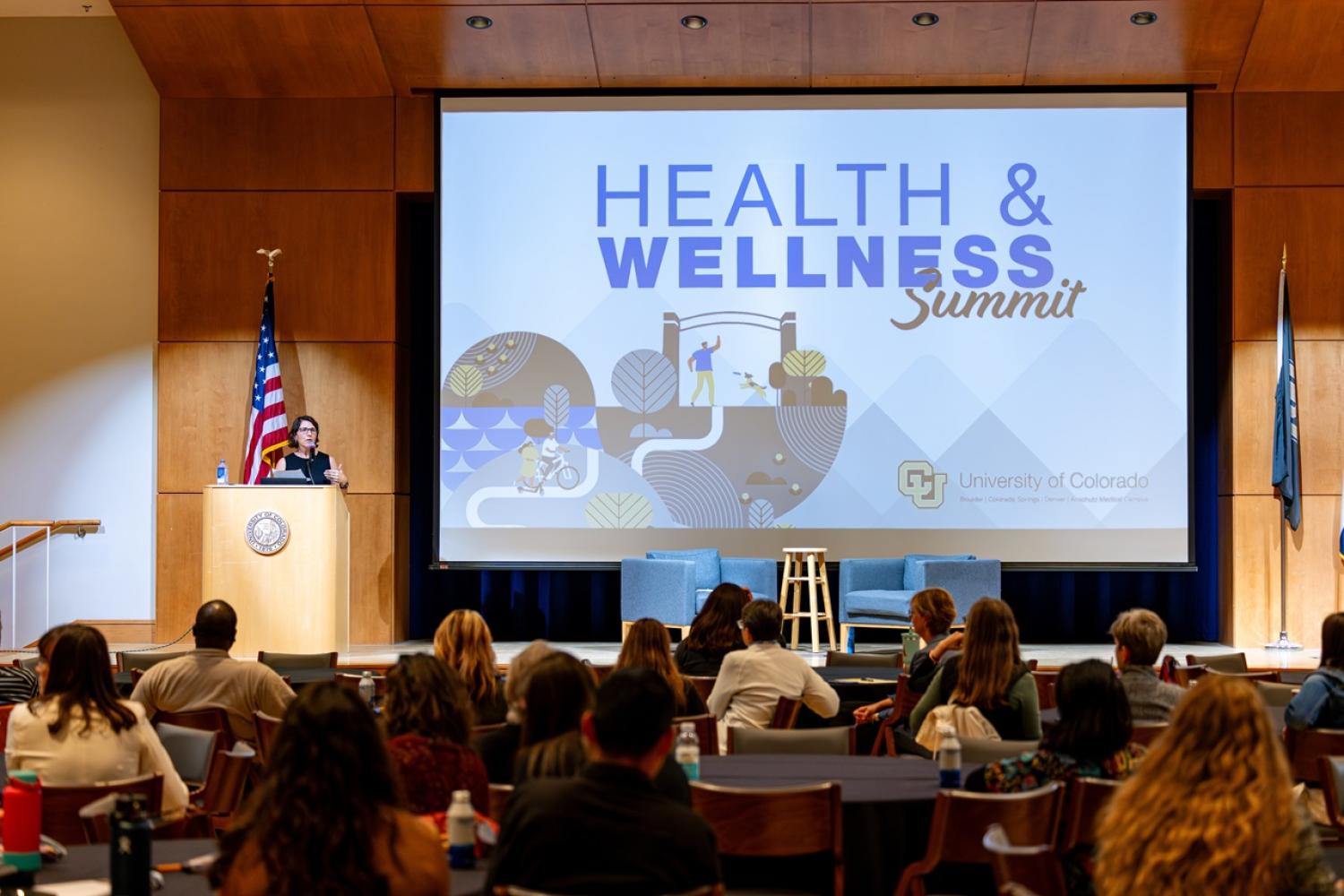 Health & Wellness Summit Logo projected on a screen in an auditorium.