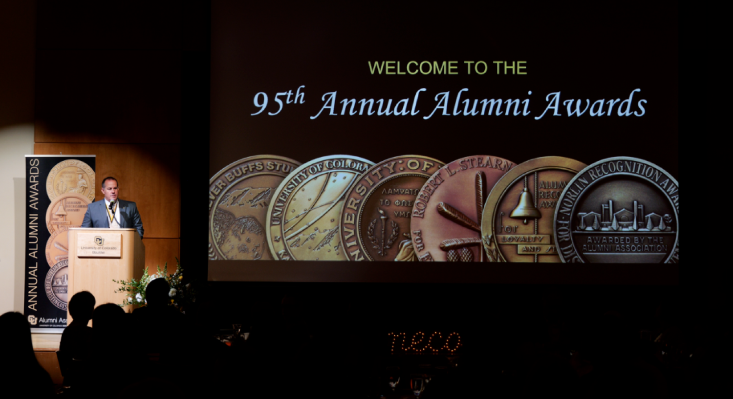 text written " Welcome to the 95th Annual Alumni Awards" with various coins below