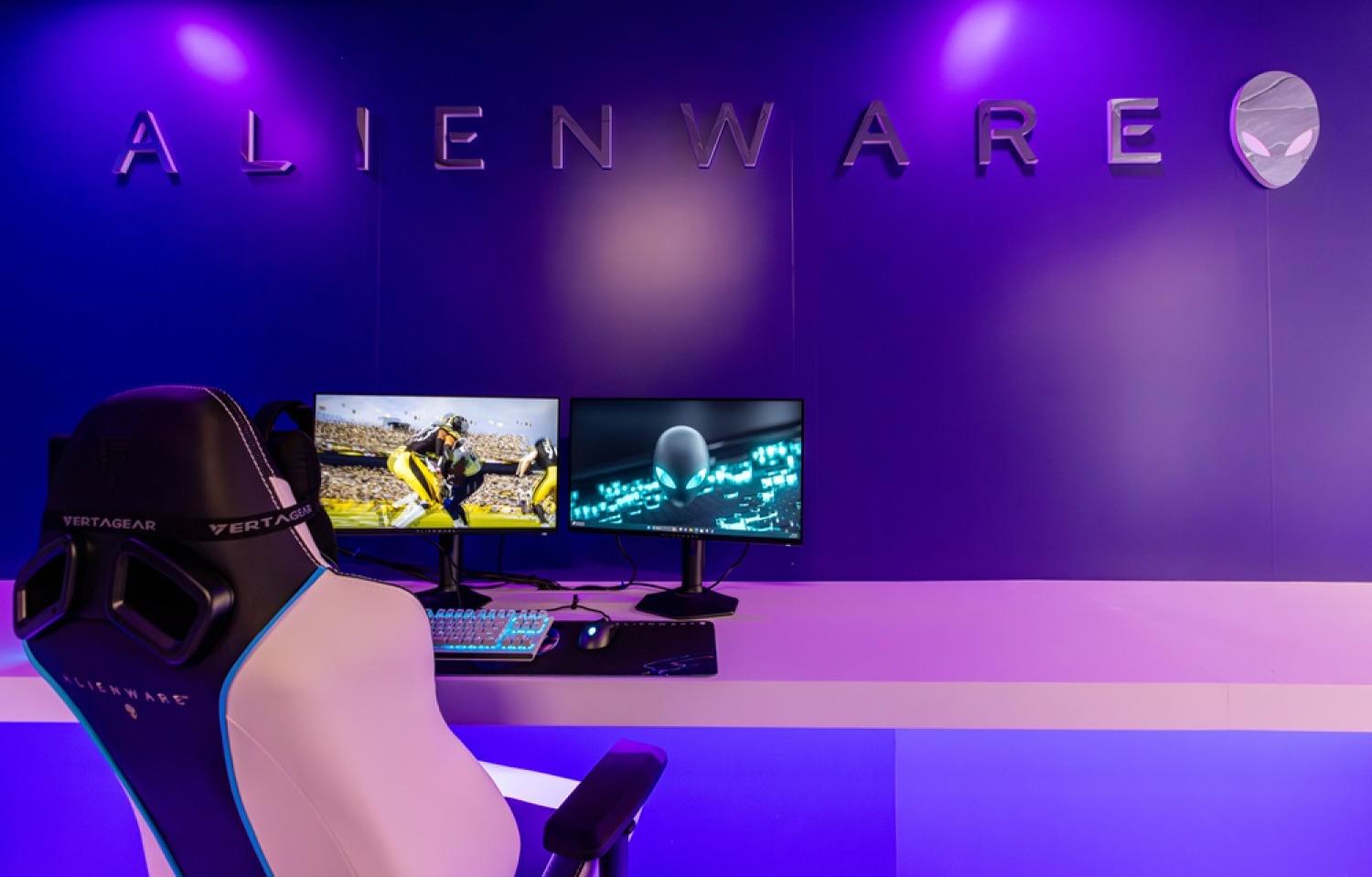 Gaming Chair and dual monitors in a pink and purple lit room with "Alienware" on wall