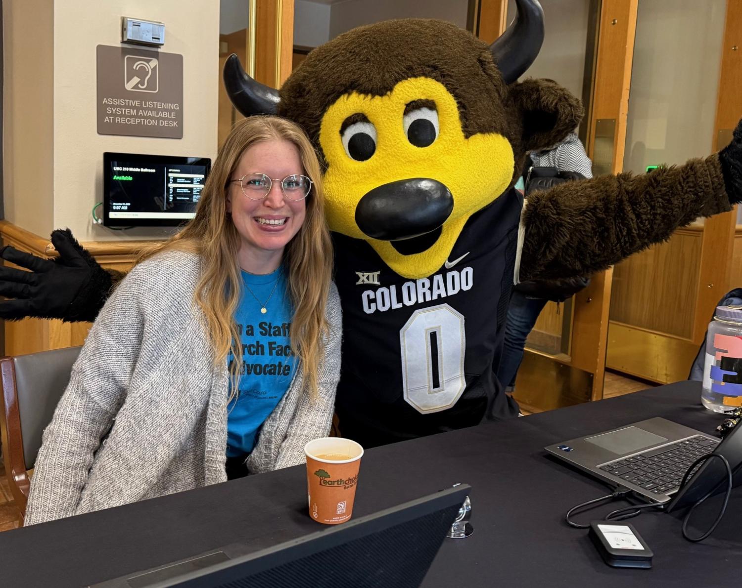 Staff council member sitting at check in desk with CU Mascot Chip