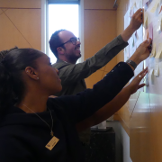 Two staff council members putting sticky notes on a board
