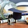 Glass jar spilling out with money and graduation cap