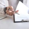 Hand with pen flipping through papers on a clipboard