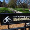Student riding a bike past Be Boulder. sign