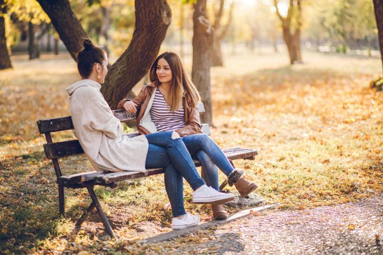 Two people talking on a bench outside