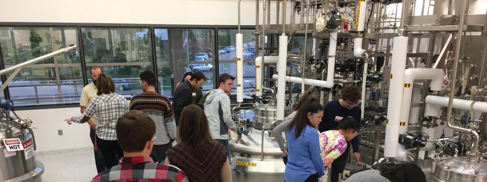 Students peer into machinery at the AstraZeneca manufacturing facility.