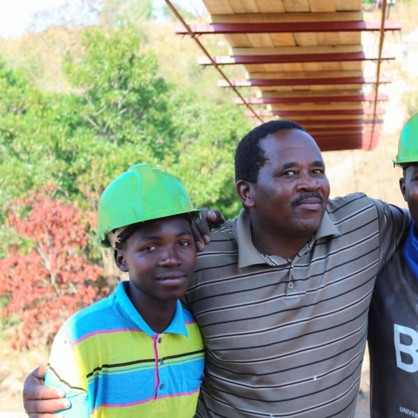 Three men with hard hats on, standing under bridge