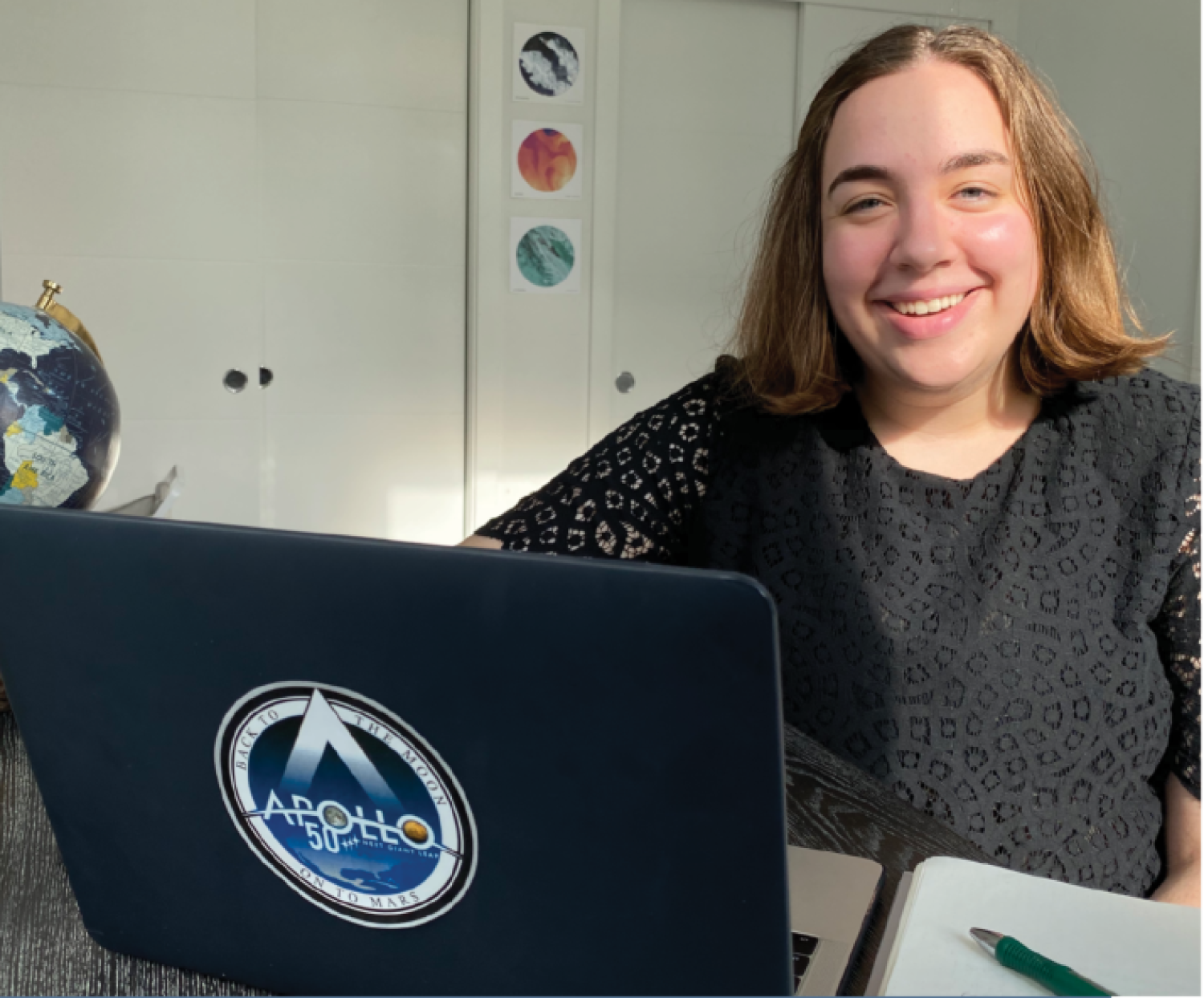 Hanna Galimanis sitting at her desk behind her laptop that is proudly displaying an Apollo 50yr sticker. She is smiling.