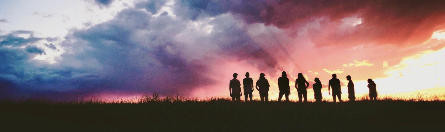 Silhouette of people in field with sunrise in background