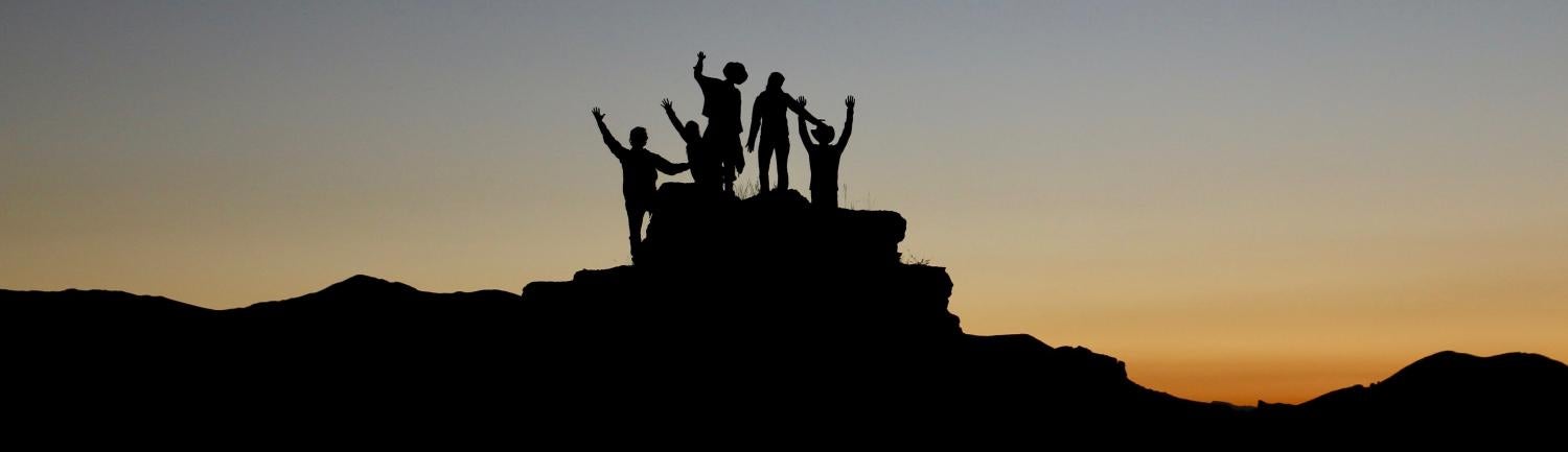 Silhouette of people on rock with background sunset
