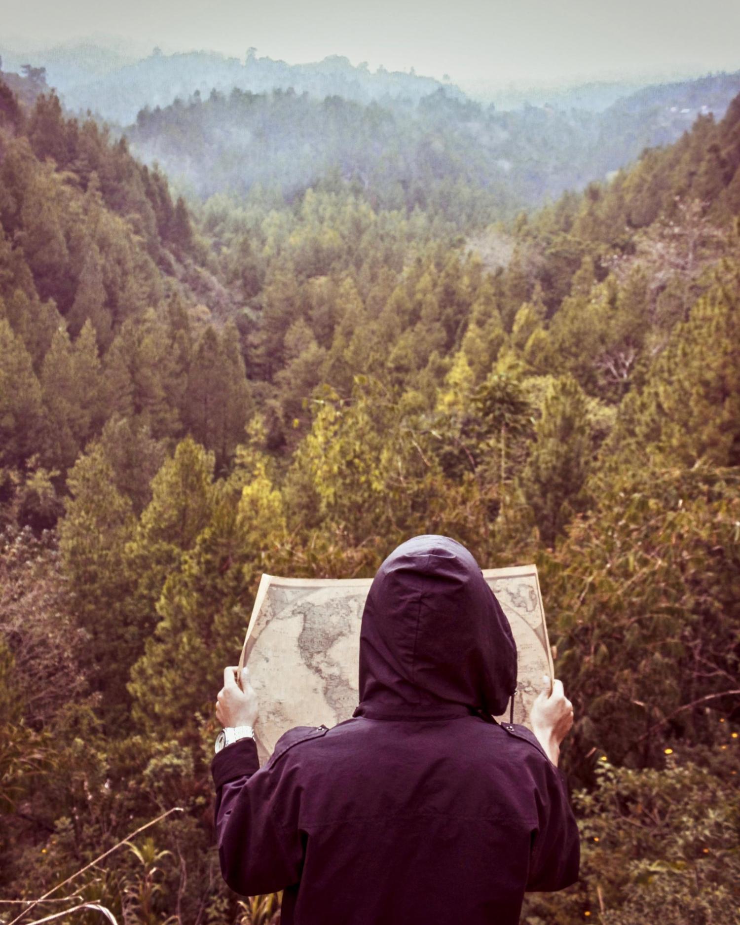 Hooded person looking at map in front of forest valley