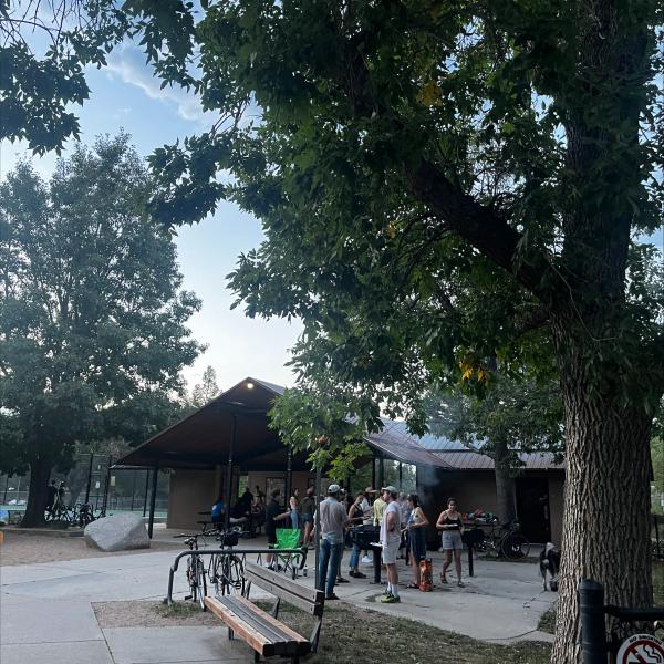 Picture of the bbq venue. There are people by a covered pavillion eating food and grilling.