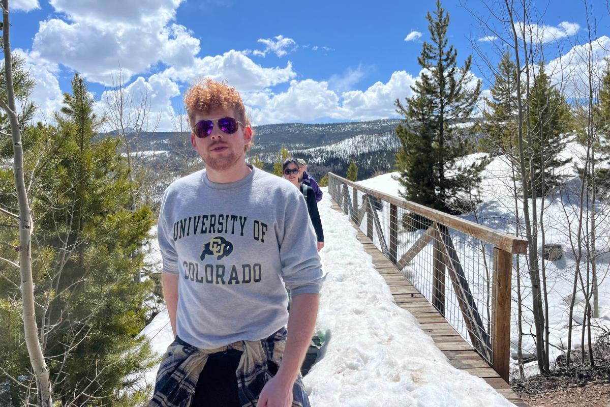 a red-haired man in cu boulder shirt in front of snowy trail and blue skye