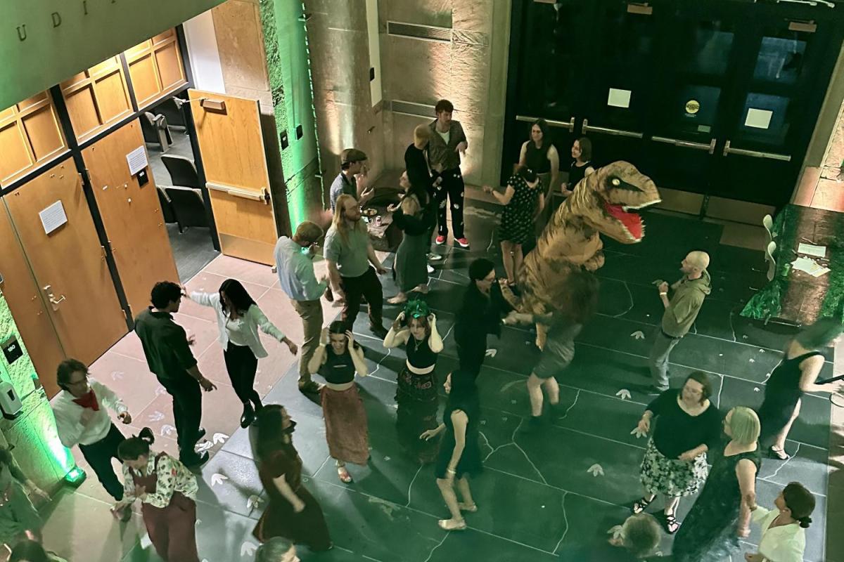 people dancing in the Benson building atrium, including someone in a t-rex costume