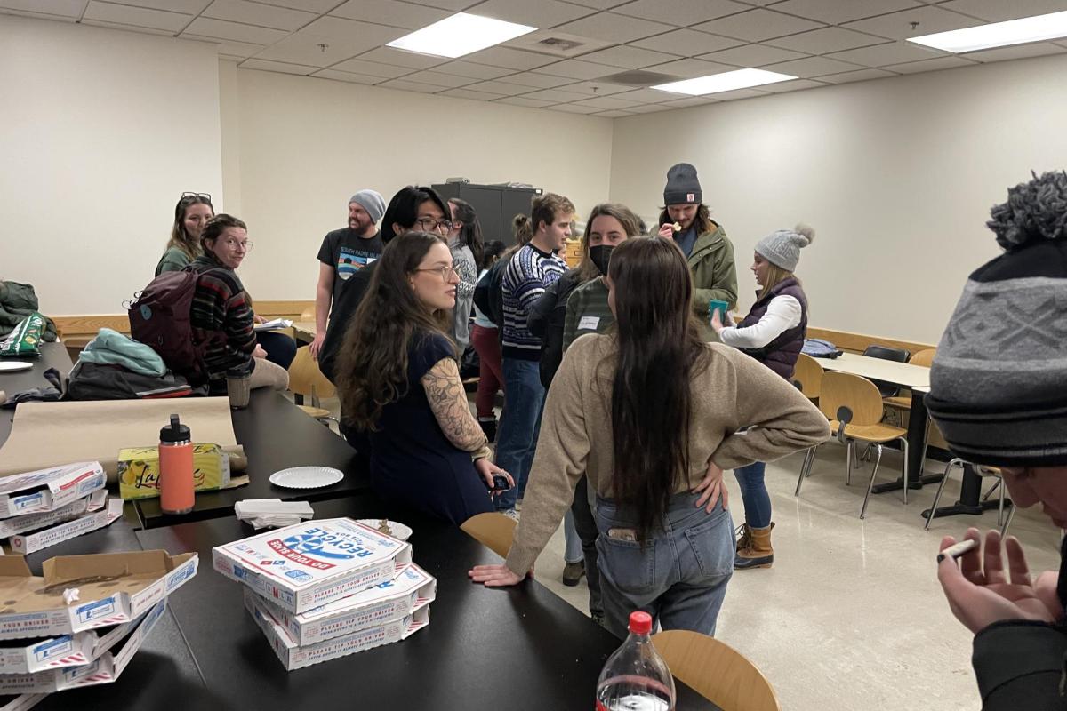 group of diverse people in their 20s standing next to table with pizza