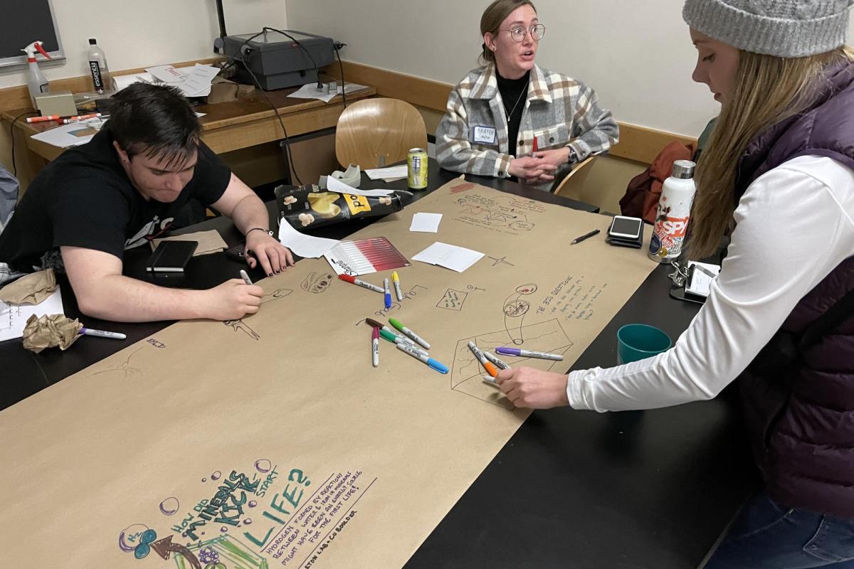 three young white people drawing on a communal piece of paper