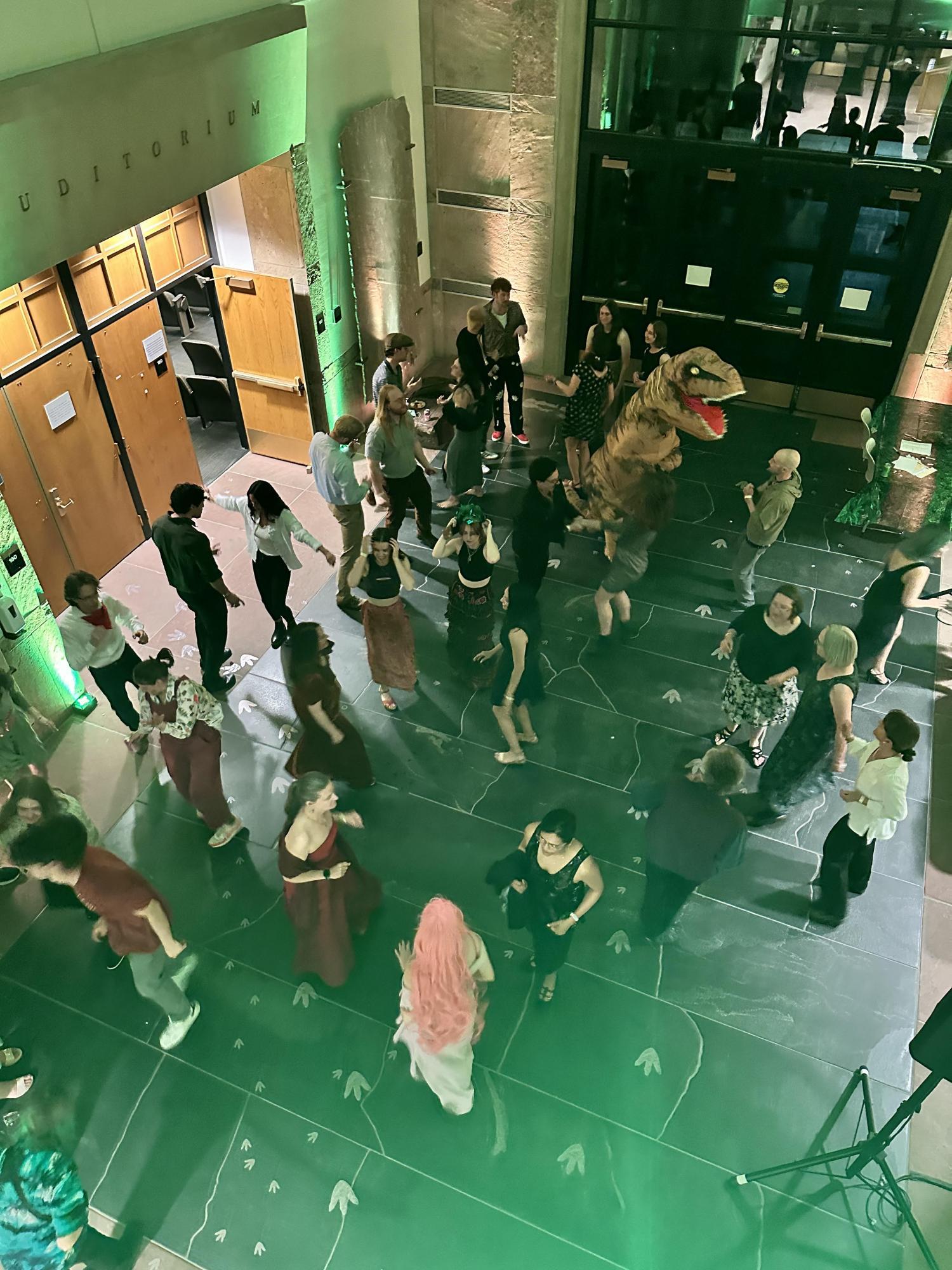people dancing in the Benson building atrium, including someone in a dinosaur costume