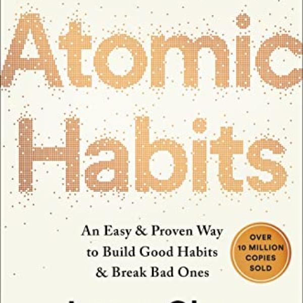 The cover of the book Atomic Habits. Small gold particles assemble to form the title against an off-white background.