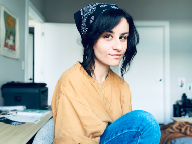 Photo of dana, a light-skinned young woman with short dark hair and wearing a baggy, orange T-shirt and a bandana