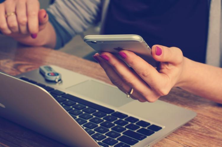 A woman holding a smart phone and sitting in front of a laptop