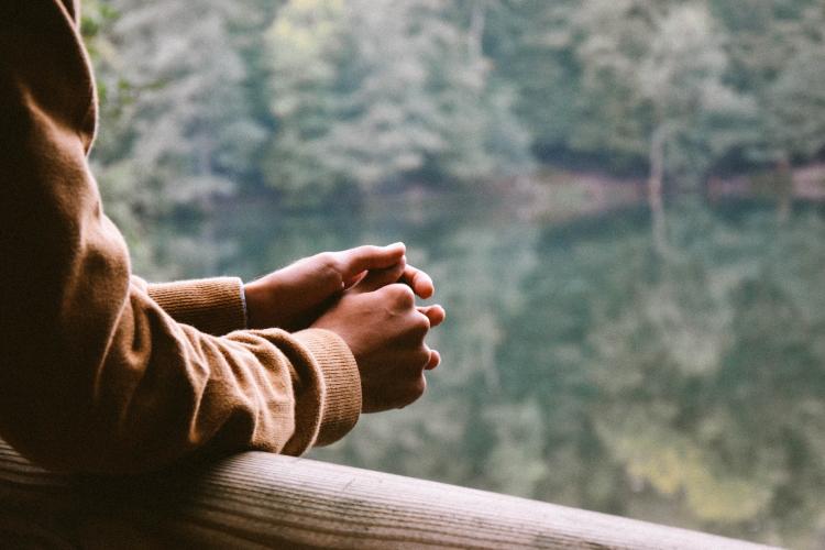 A close-up image of a person's hands as they lean on a bridge railing