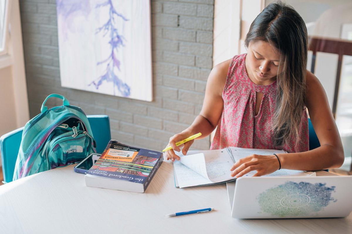 A student reads with a laptop in a light-filled home.