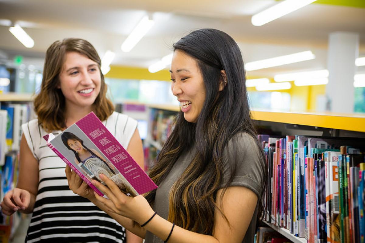 Two Education students browse children's books in a colorful library.