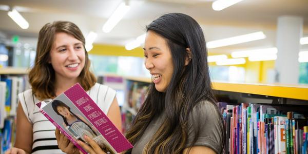 Two Education students browse children's books in a colorful library.