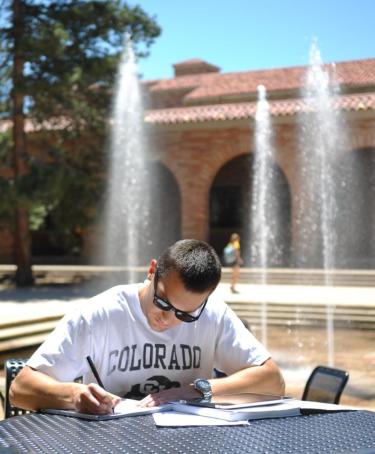 male student working outside at a table