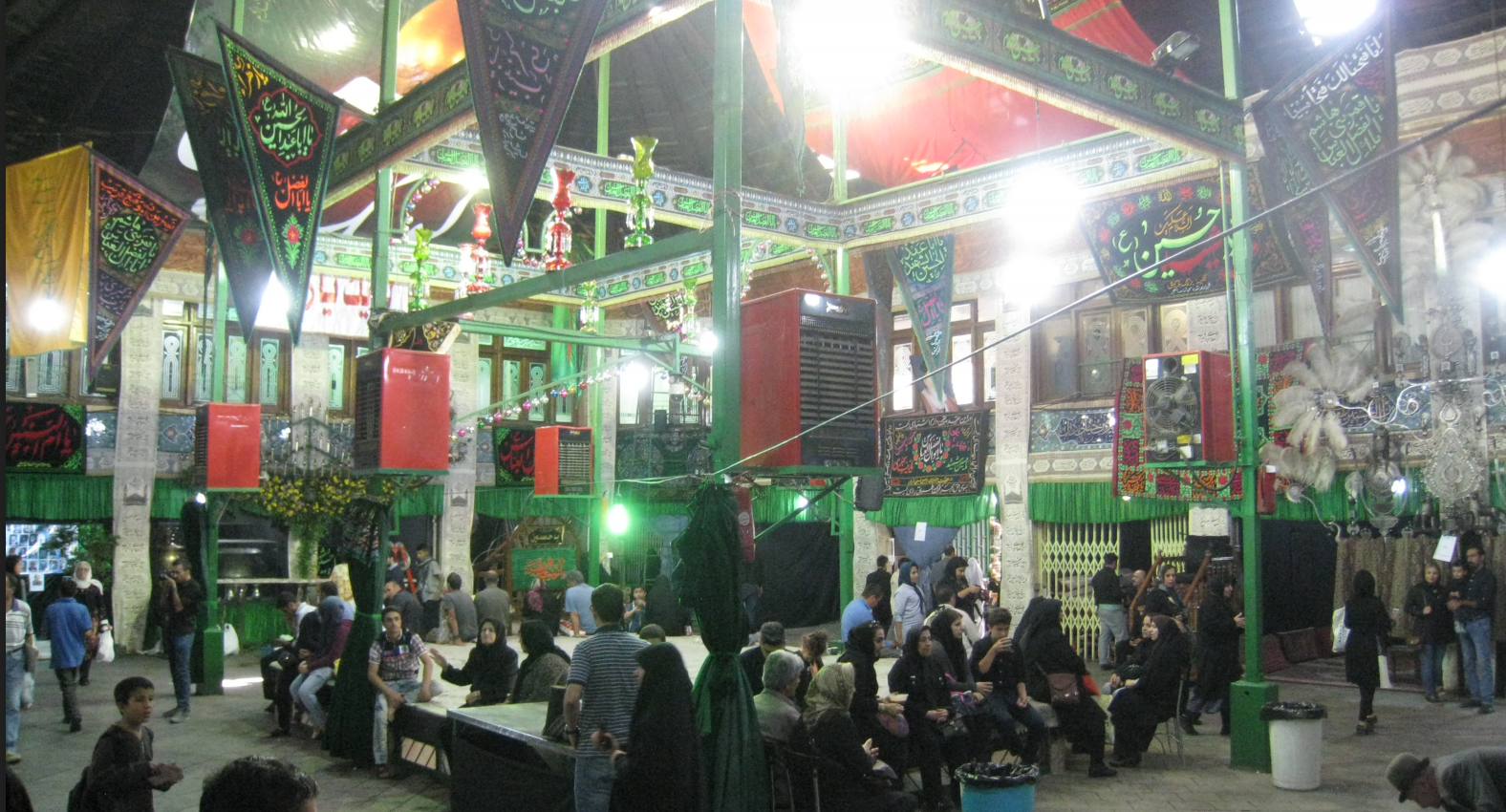 Market square, with green poles and hanging triangular flags, filled with people