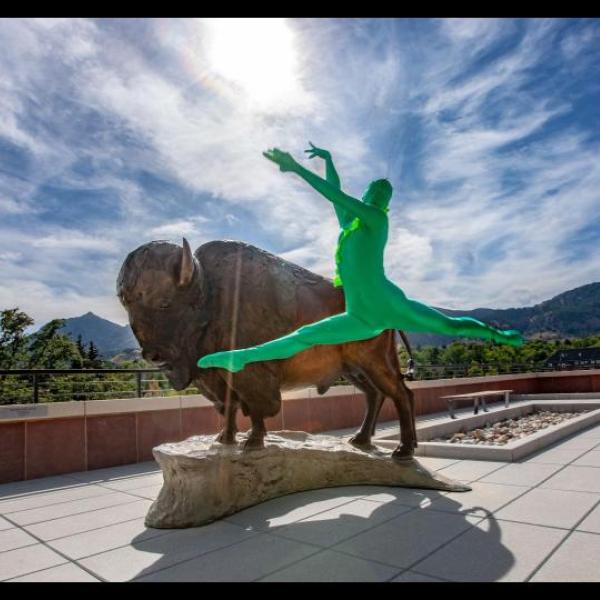 Person in a green suit leaping in front of a Ralphie statue