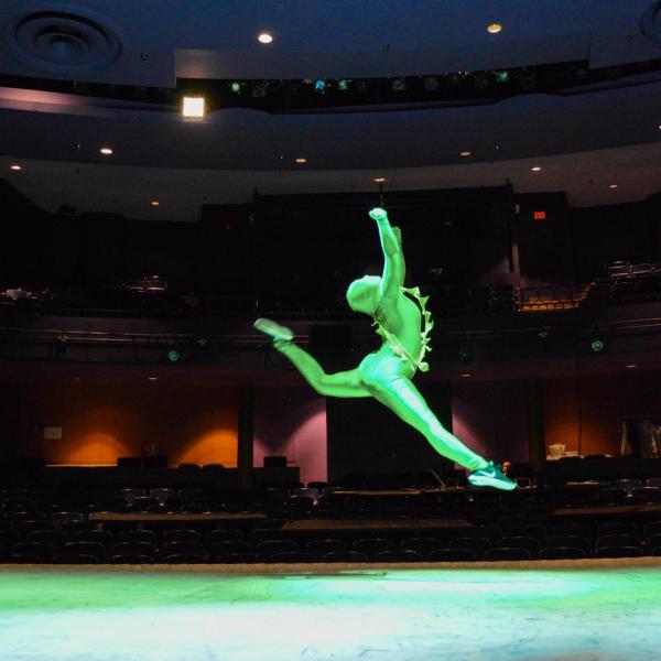 Person in a green suit jumping on the University Theatre stage 