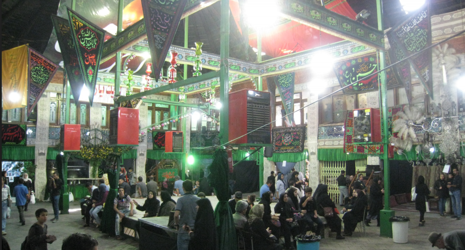 Market square, with green poles and hanging triangular flags, filled with people
