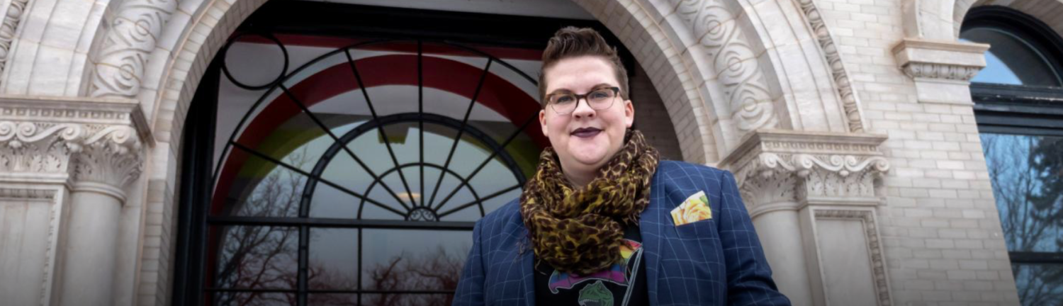 Woodzick standing in front of glass window with dinosaur shirt and blue jacket