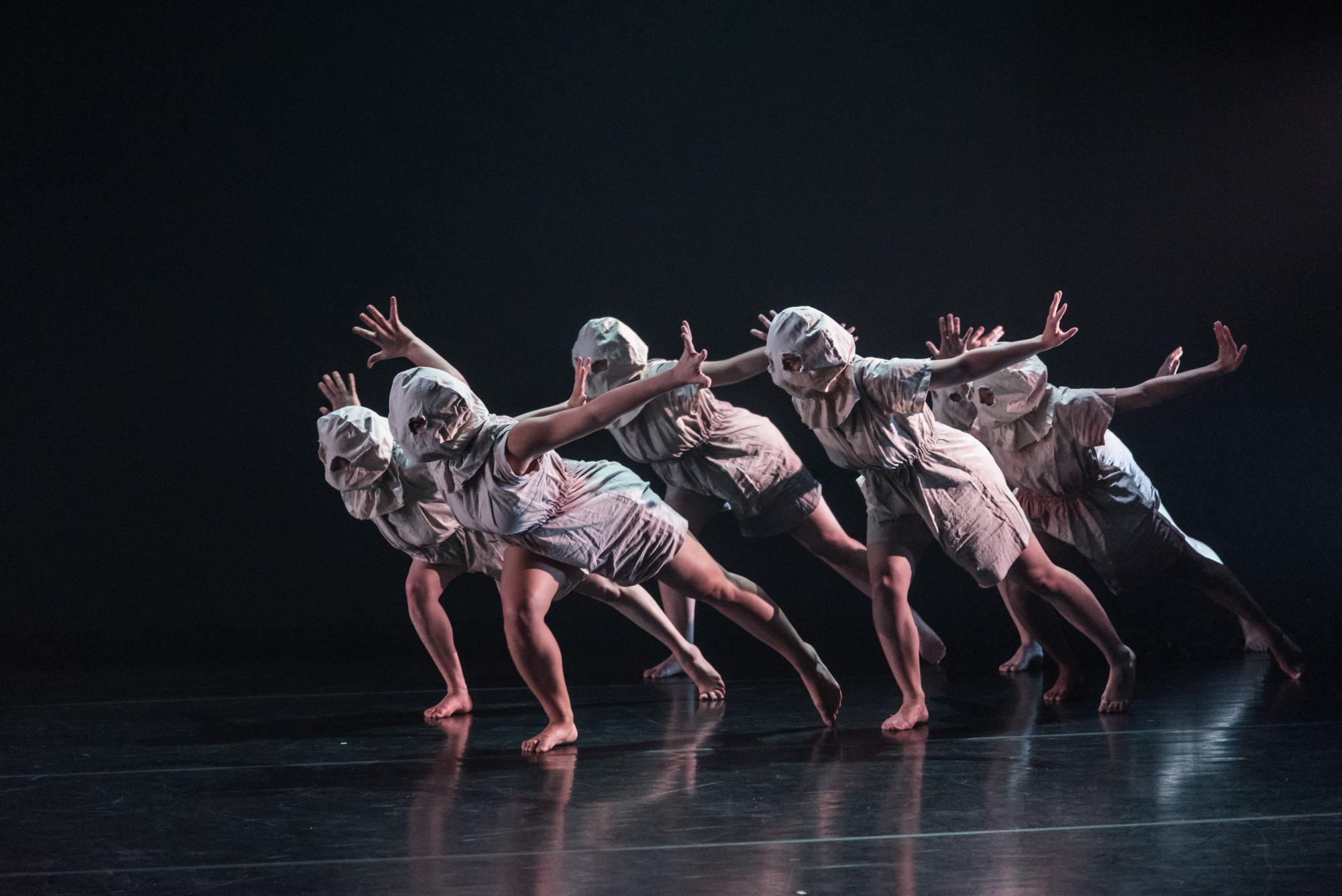Five masked dancers move onto the stage