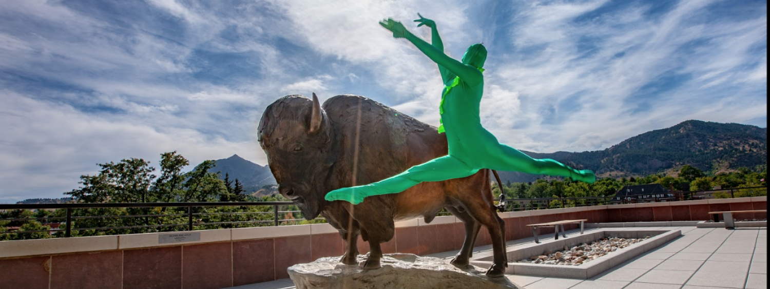 Person wearing a green suit leaping in front of a statue of Ralphie