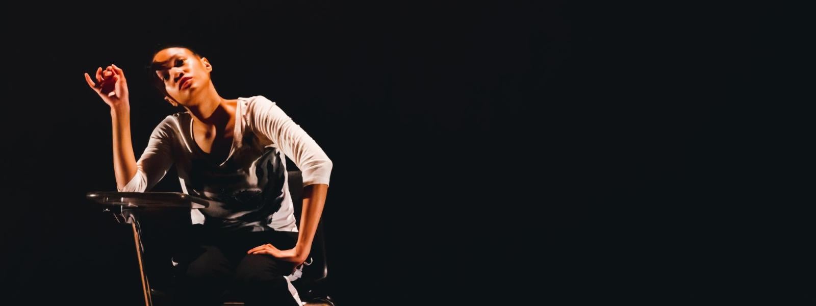 A dancer sits at a desk, alone on stage