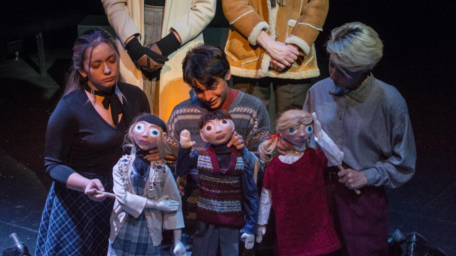 Three students hold dolls and kneel before two others who look on