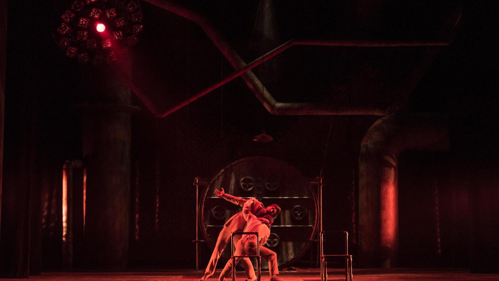 two actors fight on a stage with red light
