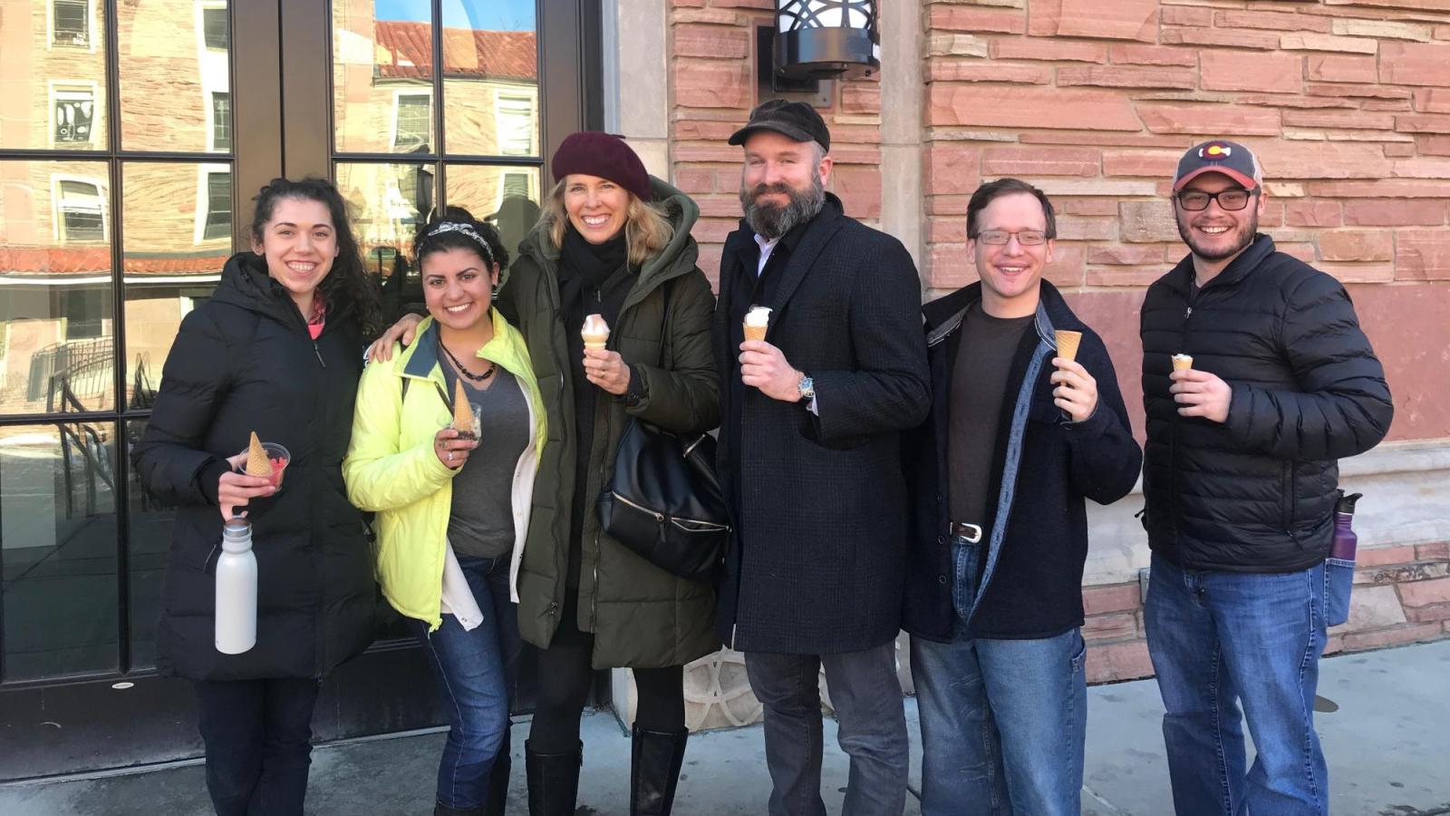 A group of students and a guest artist pose for a photo together while eating ice cream