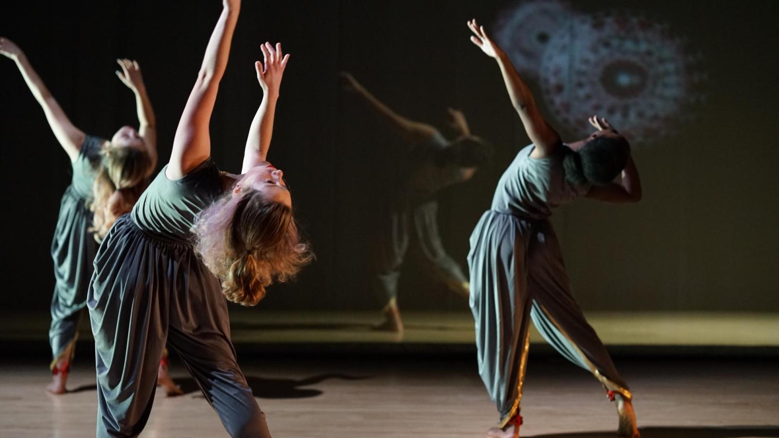 dancers on stage, leaning back while reaching up to the ceiling