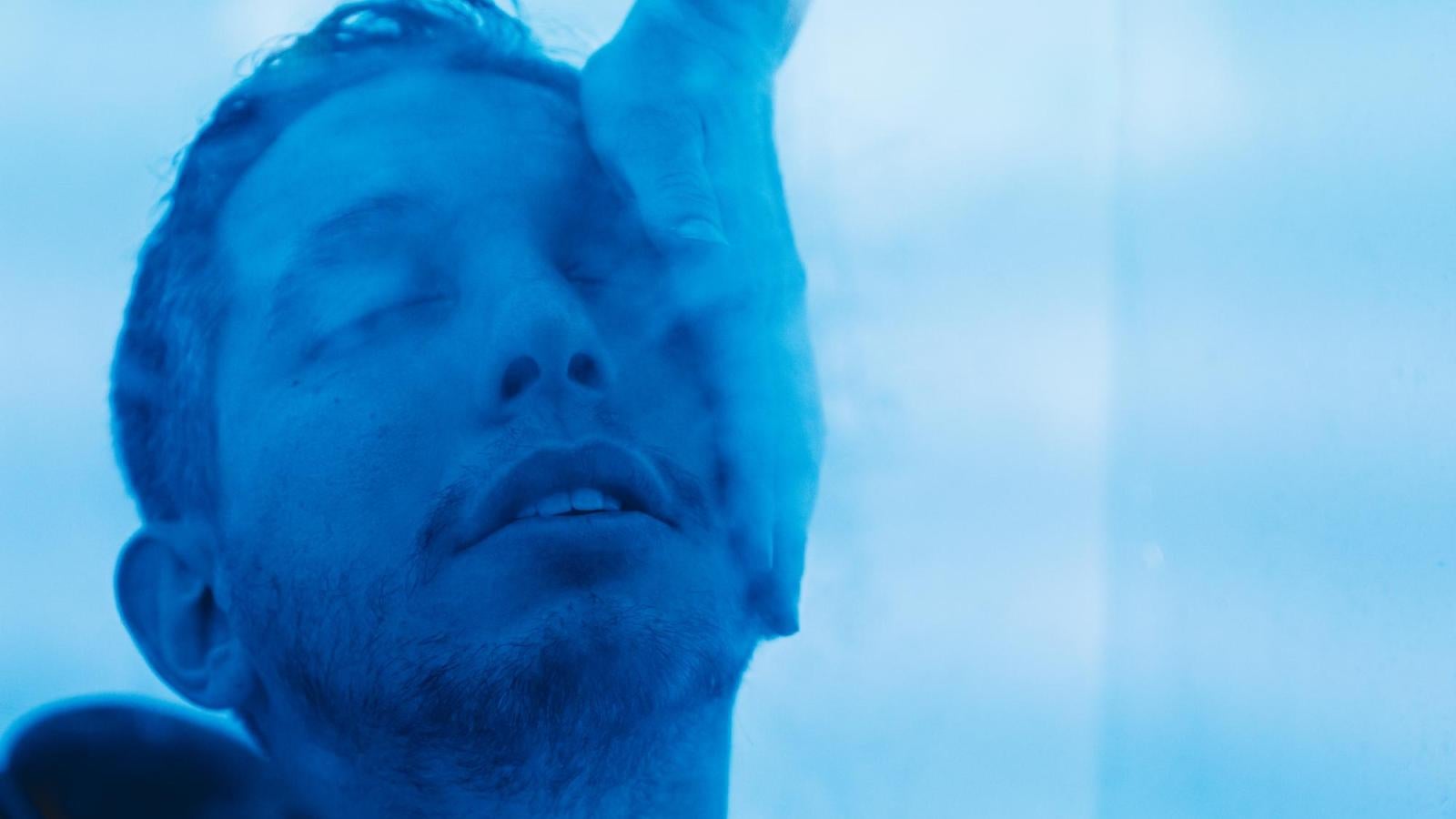 A person touches a man's face, and the man is shrouded in a blue haze