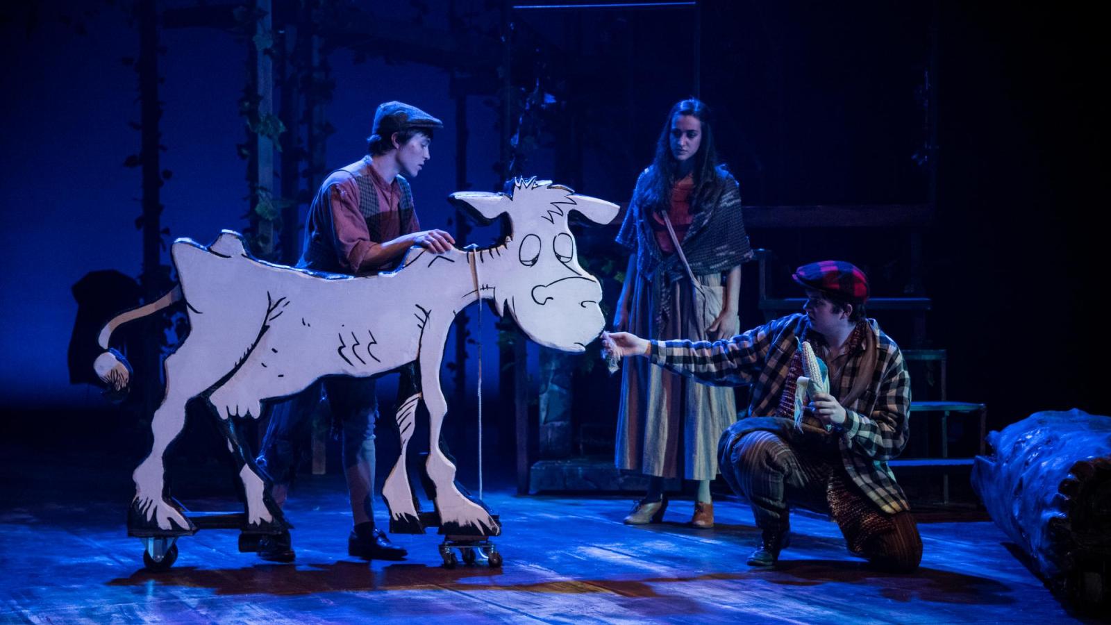 An actors feeds corn to a wooden cow