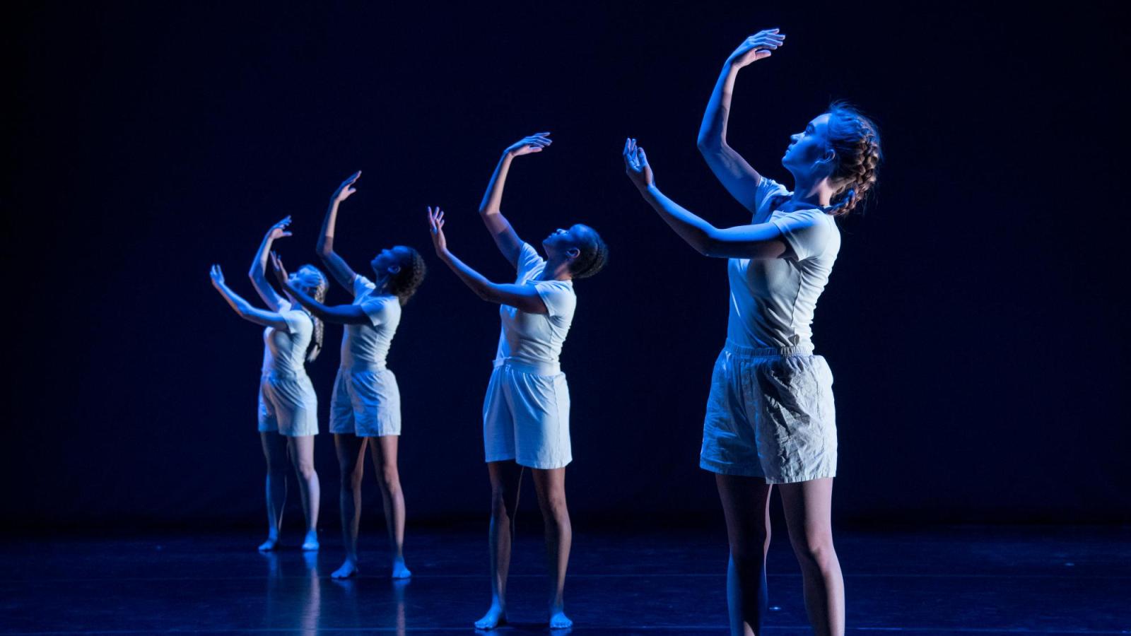 Four dancers in a line with their arms up
