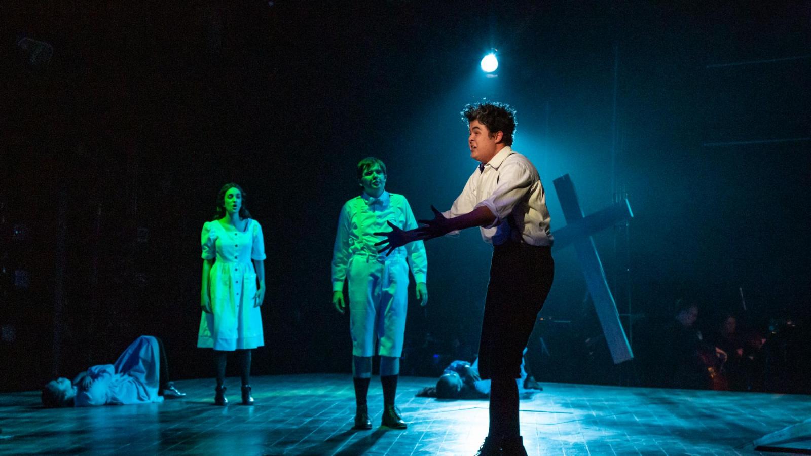 A student actor sings passionately while two others watch