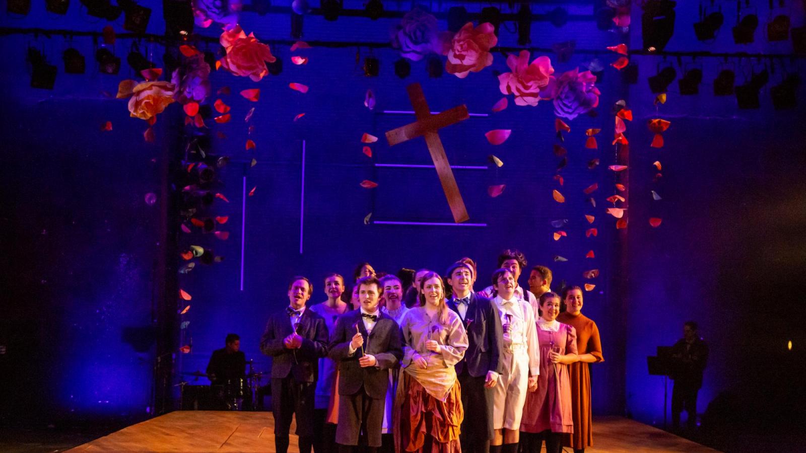 students singing onstage in front of a cross hanging from the ceiling